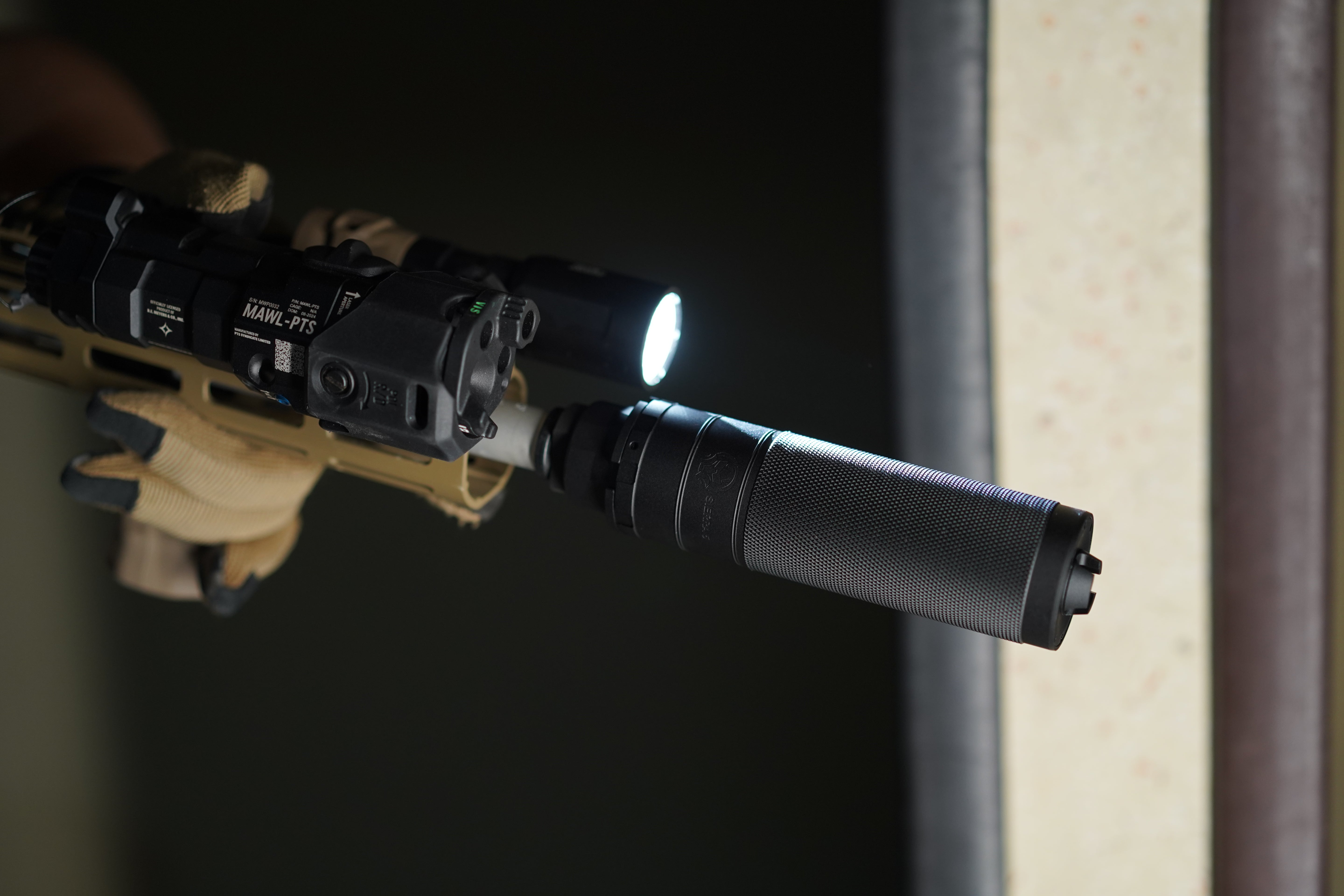 Close-up of a tan rifle equipped with a PTS Dead Air Sierra 5 Mock Suppressor, a tactical light, and other accessories.